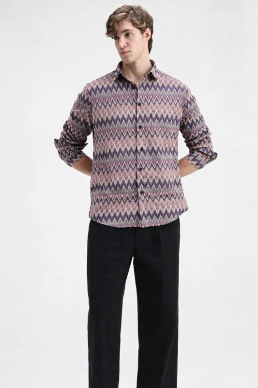 Man wearing a patterned shirt and black pants on a white background