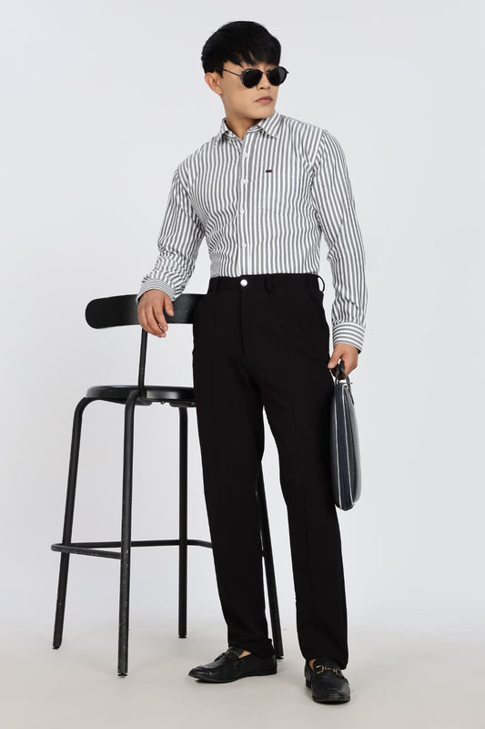 Man in a striped shirt and black pants standing next to a black stool on a white background
