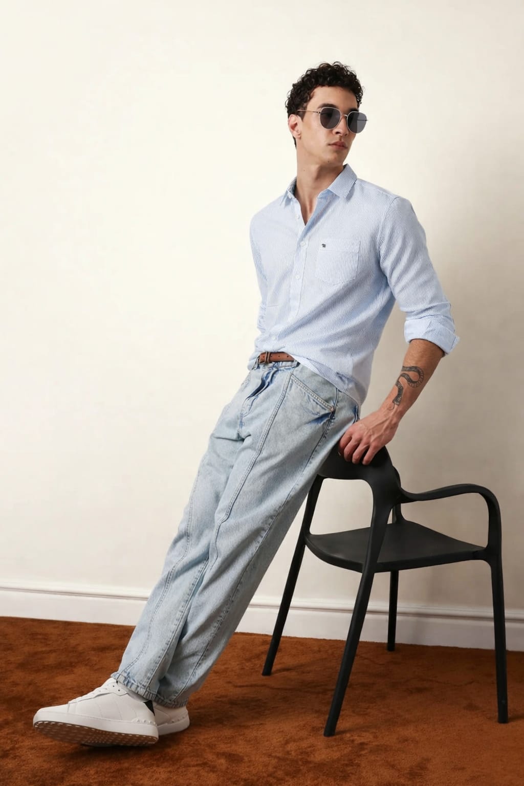 Man wearing a light blue shirt and jeans leaning against a black chair.