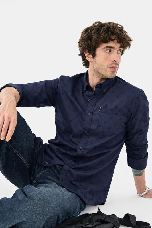 Man wearing a navy blue shirt and jeans sitting on a white background