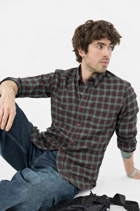 Man wearing a plaid shirt and jeans sitting on a white background