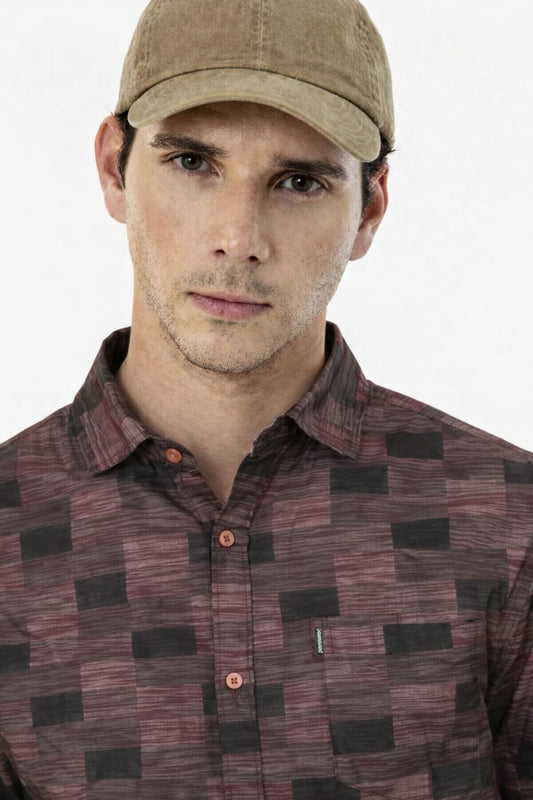 Man wearing a patterned shirt and cap on a white background