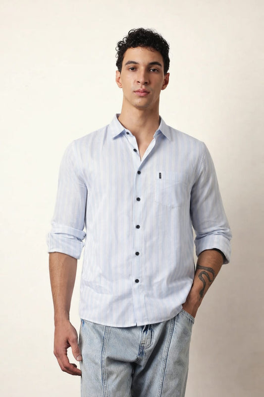 Man wearing a light blue striped shirt and gray pants against a beige background