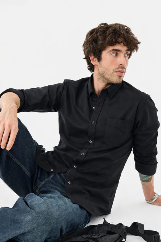 Man wearing a black shirt and blue jeans sitting on a white background