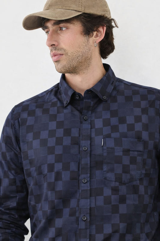Man wearing a navy and black checkered shirt with a beige cap on a white background