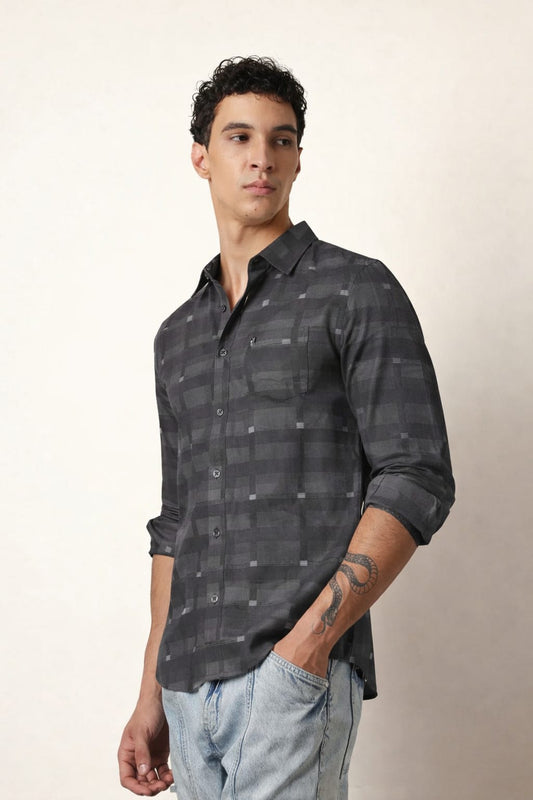 Man wearing a dark patterned shirt and light jeans against a neutral background