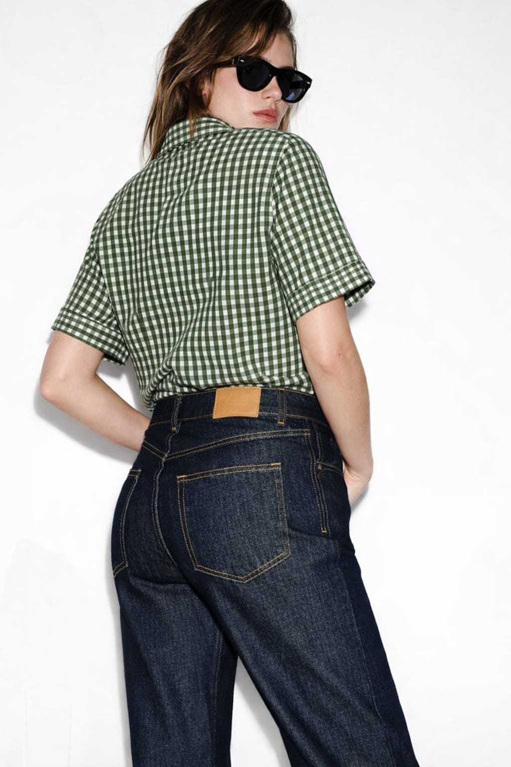 Person wearing a green checkered shirt and blue jeans against a white background