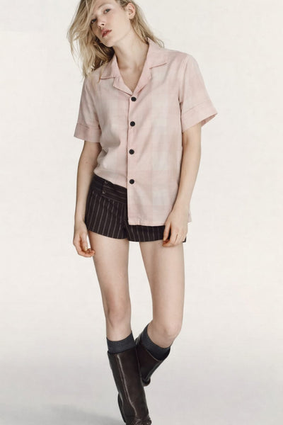 Woman wearing a light pink button-up shirt, black pinstripe skirt, and black rain boots on a white background