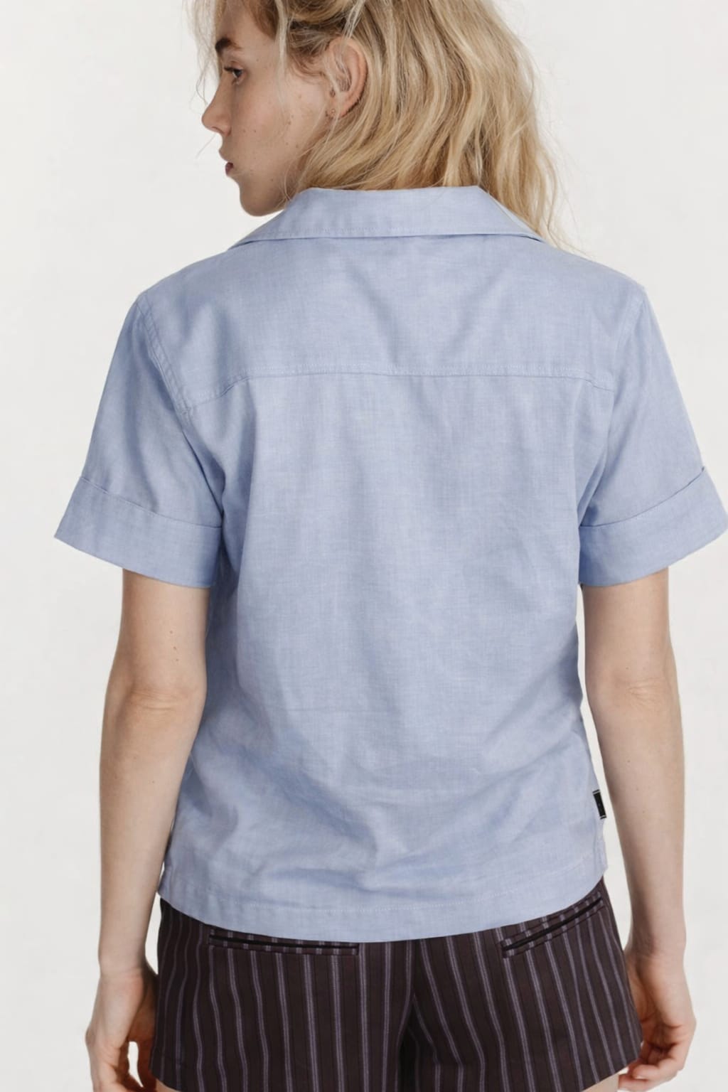 Person wearing a light blue shirt with a plain background