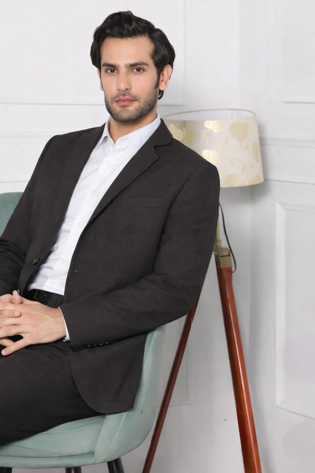 Man in a suit sitting on a chair with a lamp in the background