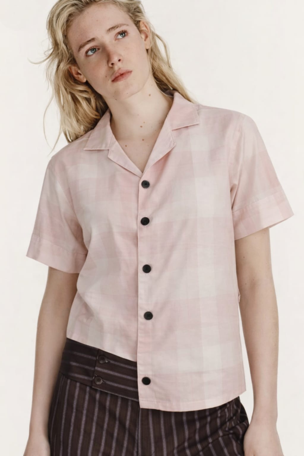 Woman wearing a light pink short-sleeve blouse with black buttons on a white background