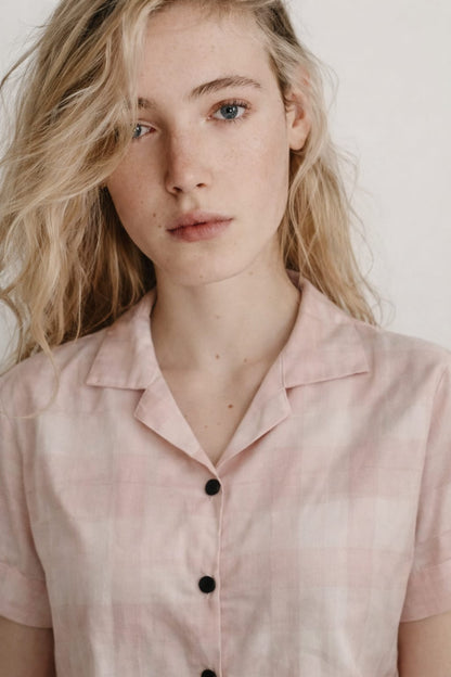 Woman wearing a light pink blouse with black buttons against a neutral background