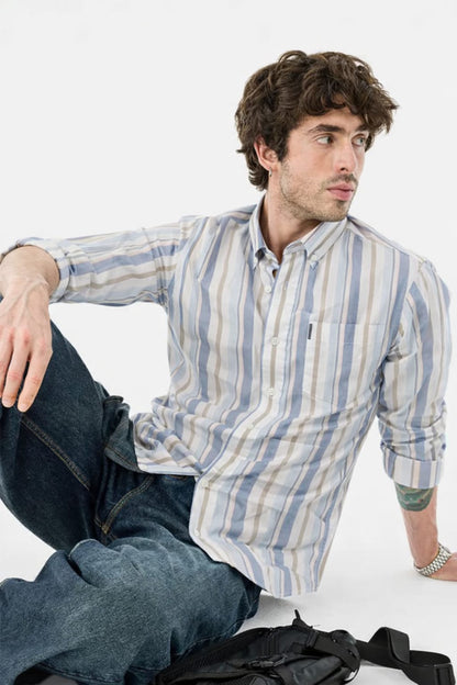 Man wearing a striped shirt and jeans sitting on the floor with a white background