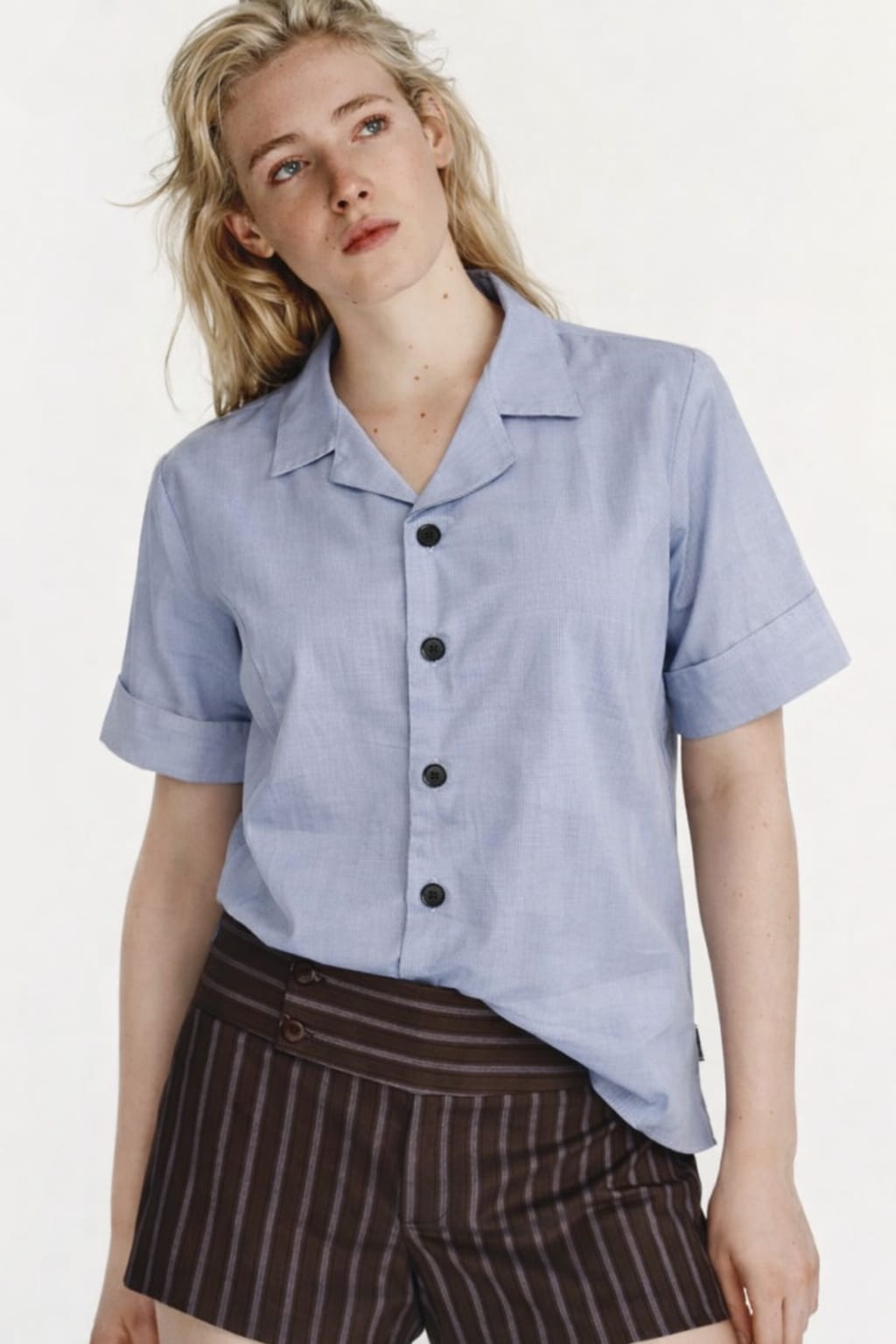 Woman wearing a light blue button-up shirt and brown striped pants on a white background