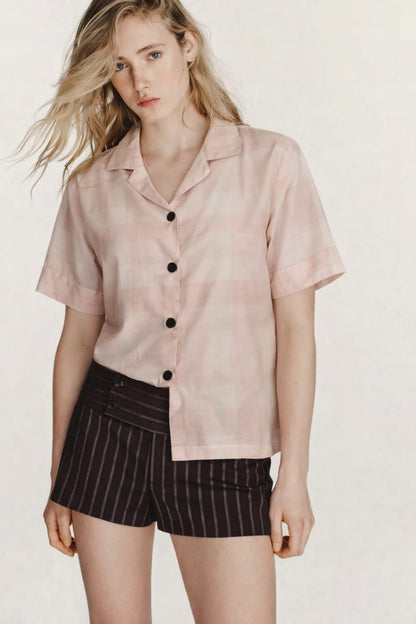 Woman wearing a light pink button-up shirt and black pinstripe shorts on a white background