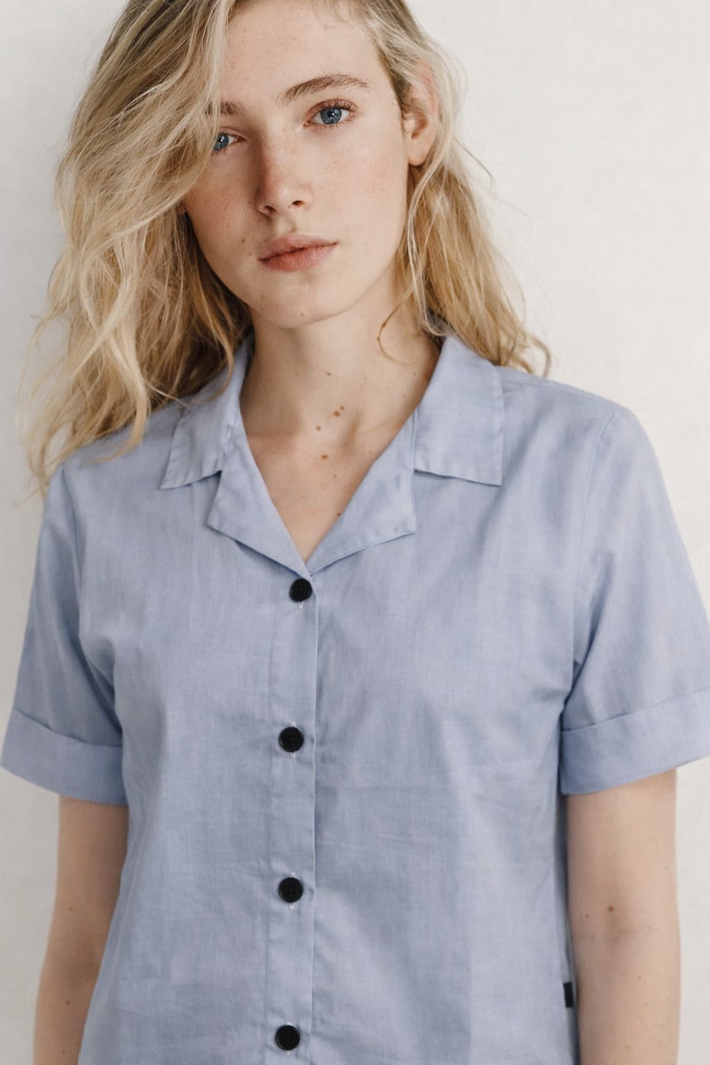 Woman wearing a light blue button-up shirt against a plain background