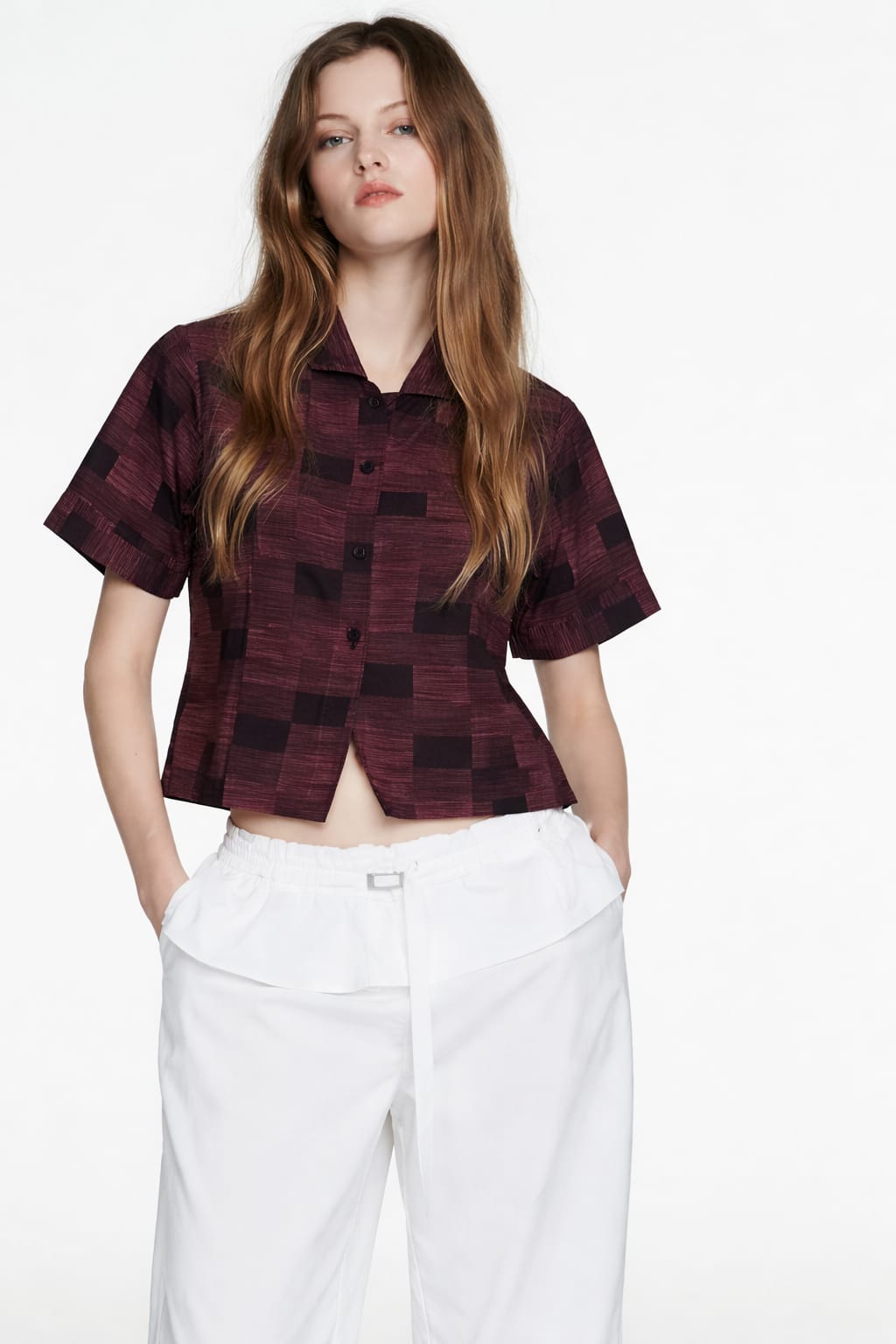Woman wearing a patterned shirt and white pants on a plain background