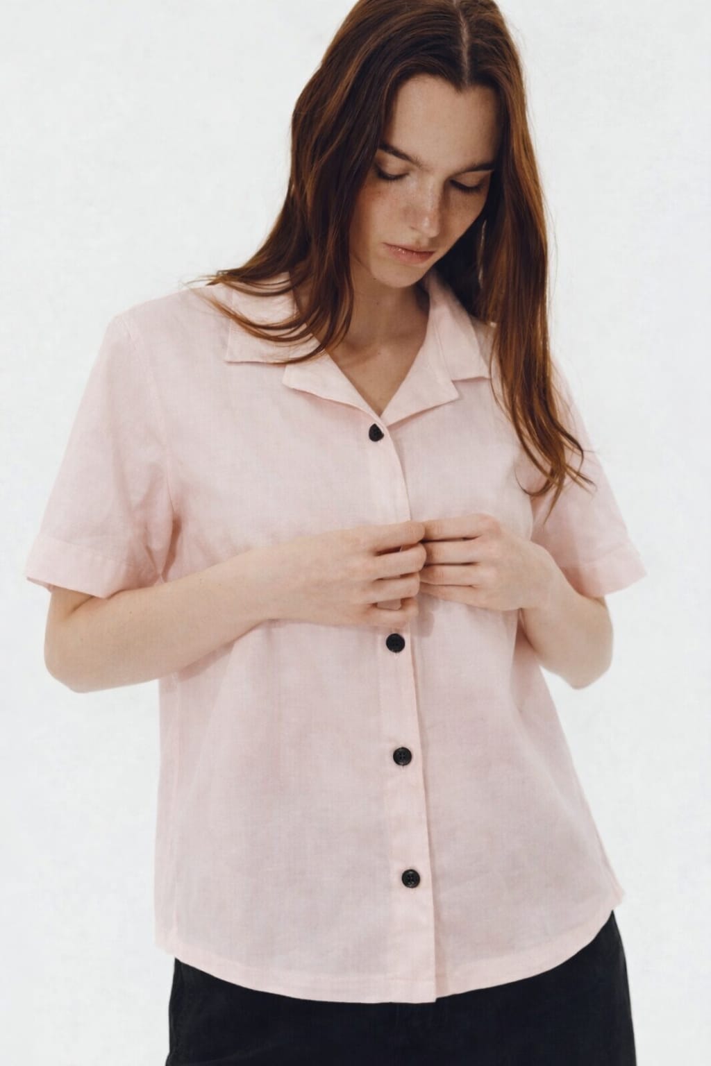 Woman wearing a light pink blouse with black buttons on a white background