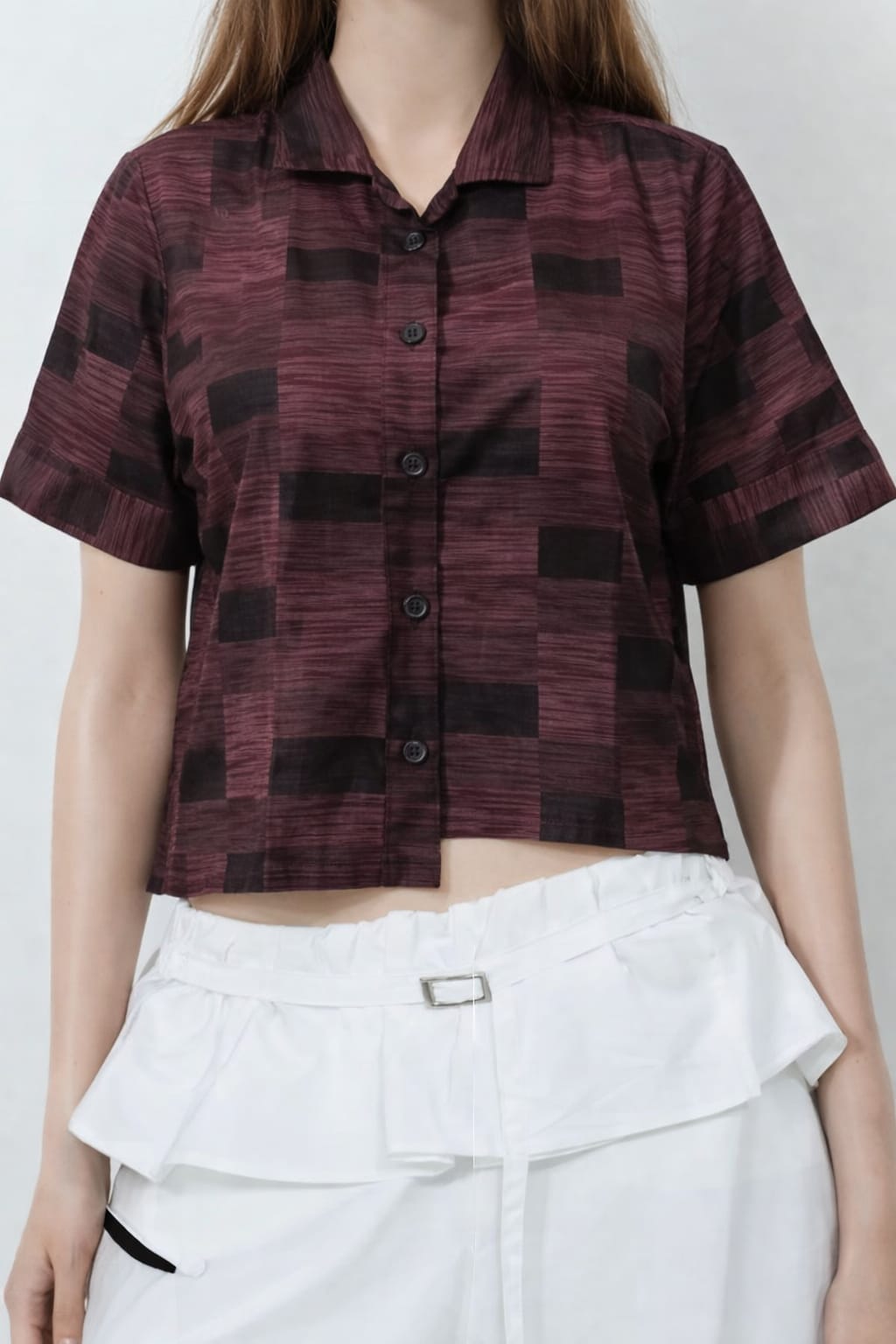 Woman wearing a patterned shirt and white pants on a plain background