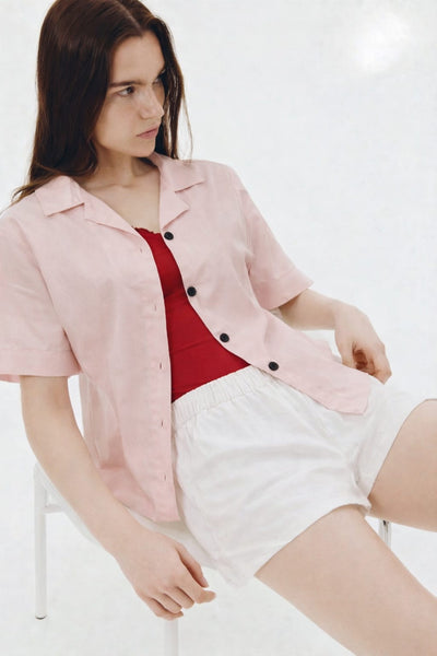Woman wearing a pink shirt over a red top with white shorts on a white background