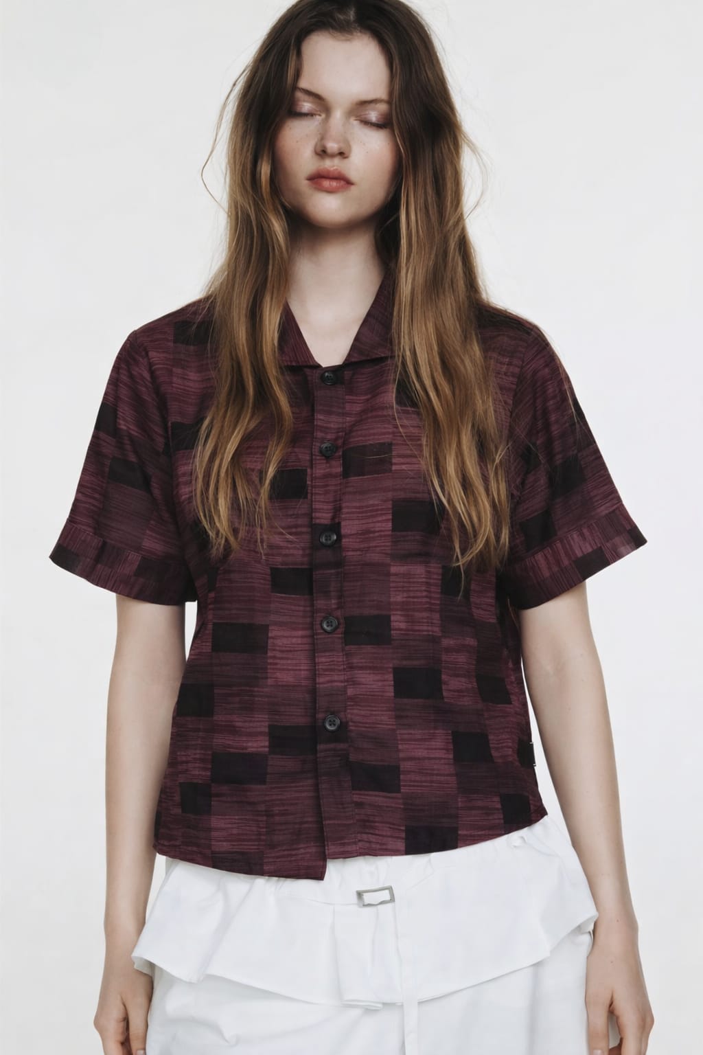 Woman wearing a patterned shirt and white pants on a plain background
