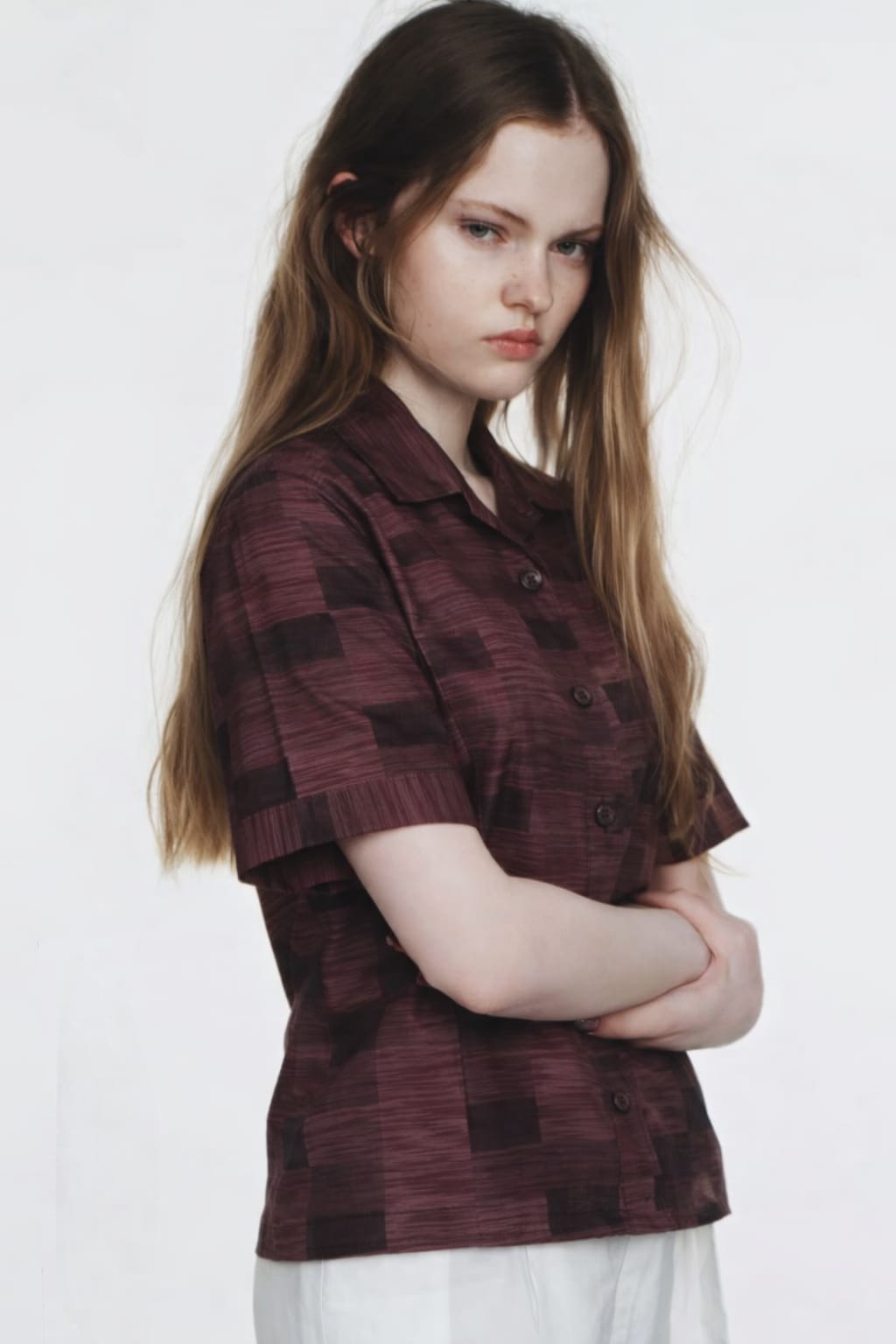 Woman wearing a patterned shirt and white pants on a plain background