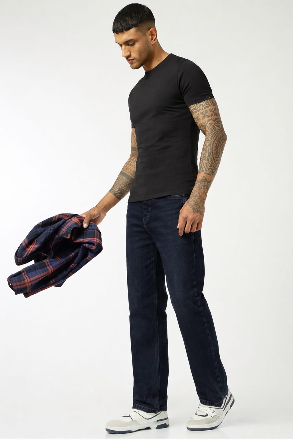 Man holding a plaid jacket, wearing a black t-shirt and dark jeans, on a white background