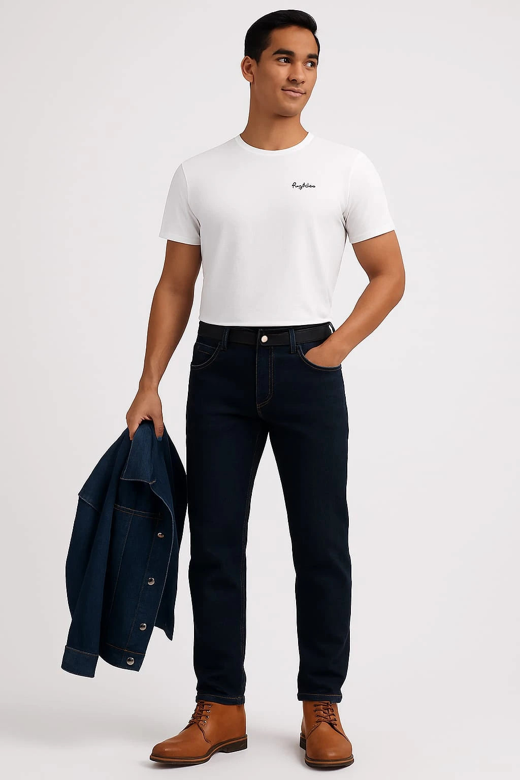 Man wearing a white t-shirt, dark jeans, and brown boots holding a navy jacket on a light gray background