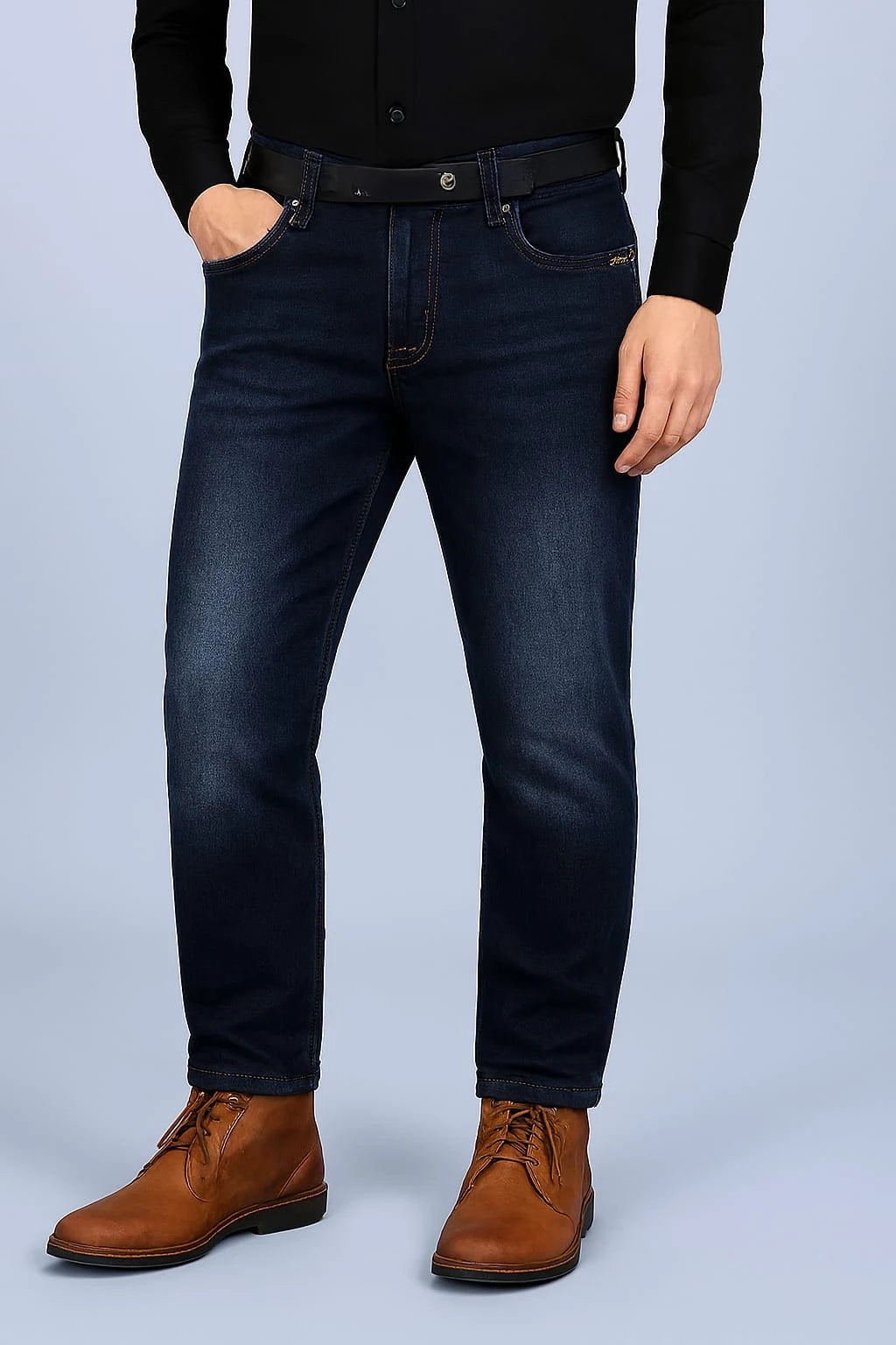 Person wearing dark blue jeans and brown shoes on a light gray background