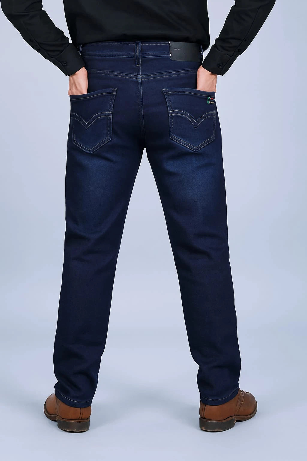 Person wearing dark blue jeans and brown shoes on a light gray background