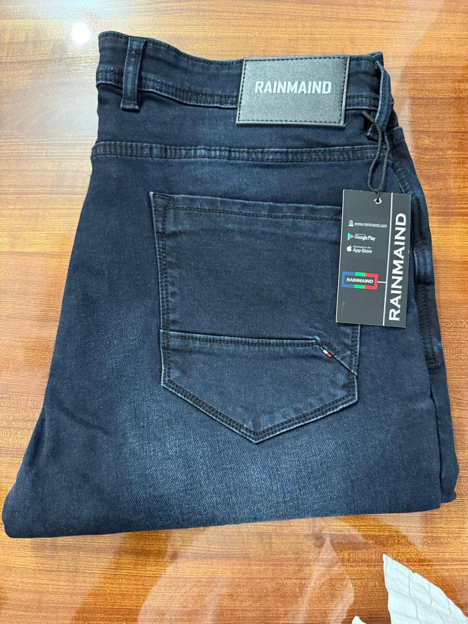 Folded blue jeans with a Rainmain label on a wooden surface