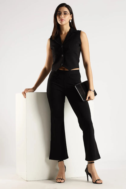 Woman in a black sleeveless top and pants posing against a white background