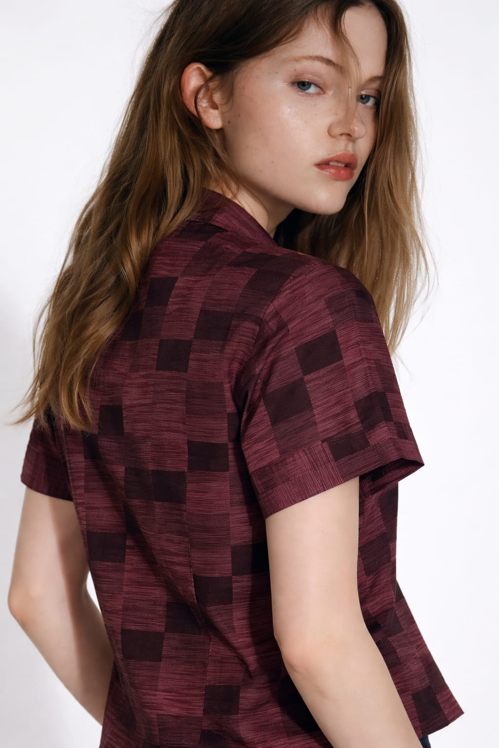 Woman wearing a patterned shirt and white pants on a plain background