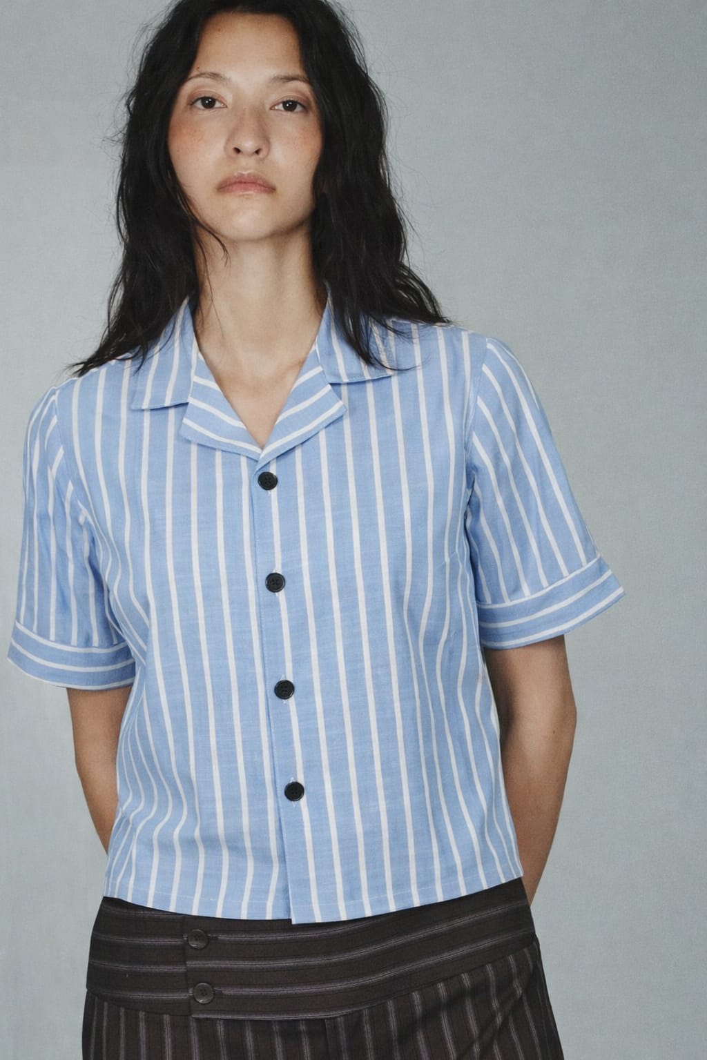 Woman wearing a blue and white striped shirt with black buttons on a gray background