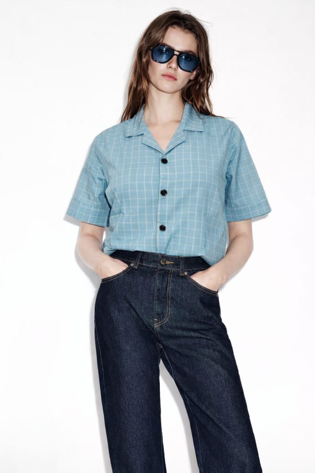 Woman wearing a blue checkered shirt and dark jeans on a white background