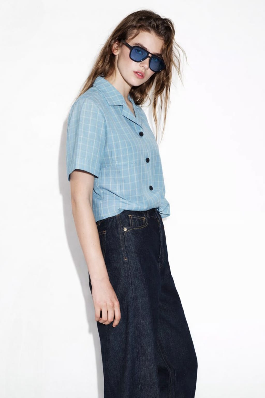 Person wearing a light blue checkered shirt and dark jeans on a white background