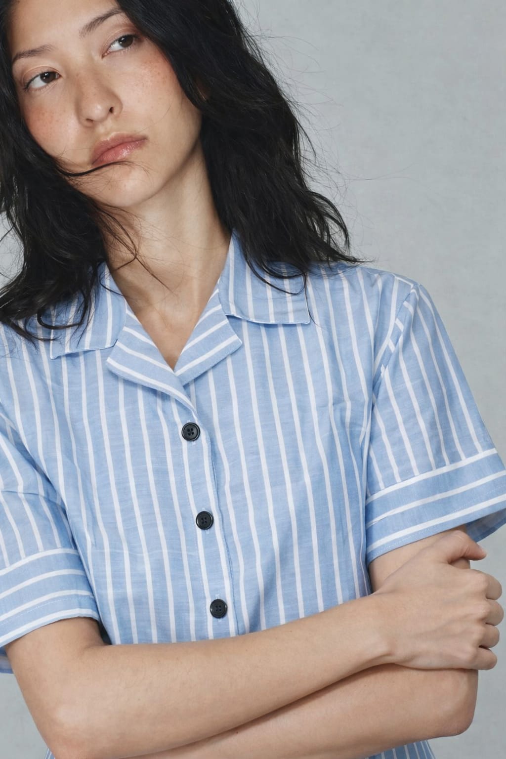 Person wearing a blue and white striped shirt with black buttons against a gray background