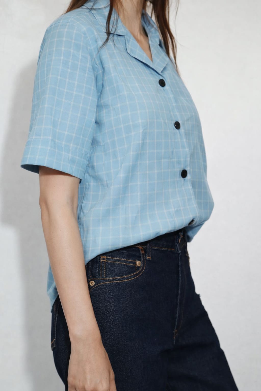 Person wearing a light blue checkered shirt and dark jeans against a white background