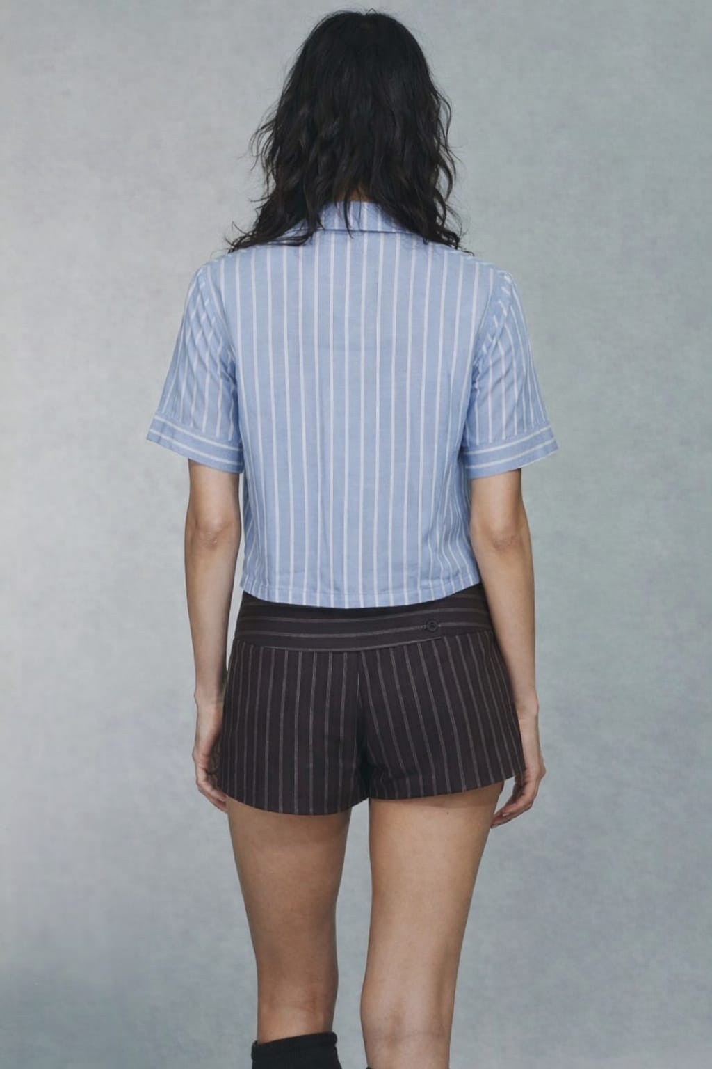 Person wearing a blue striped shirt and black pinstripe shorts on a gray background