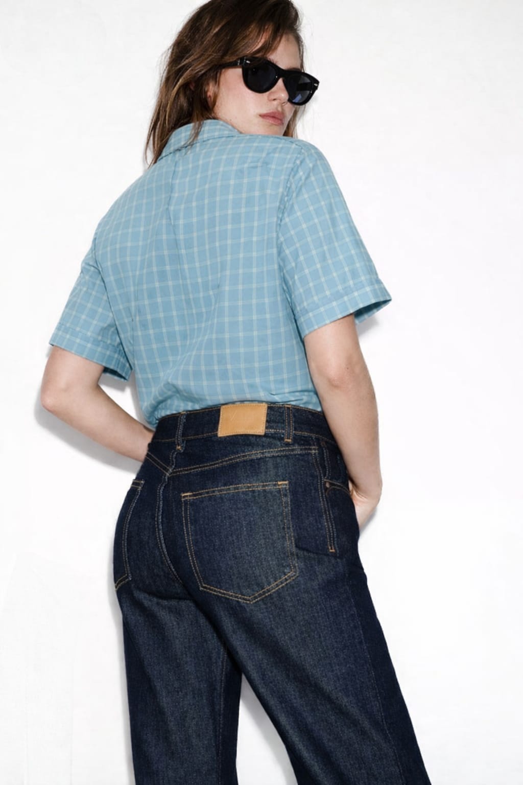 Person wearing a blue checkered shirt and dark jeans on a white background
