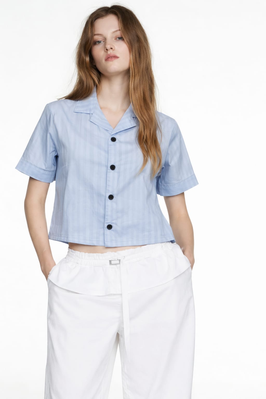 Woman wearing a light blue striped shirt with black buttons and white pants on a white background
