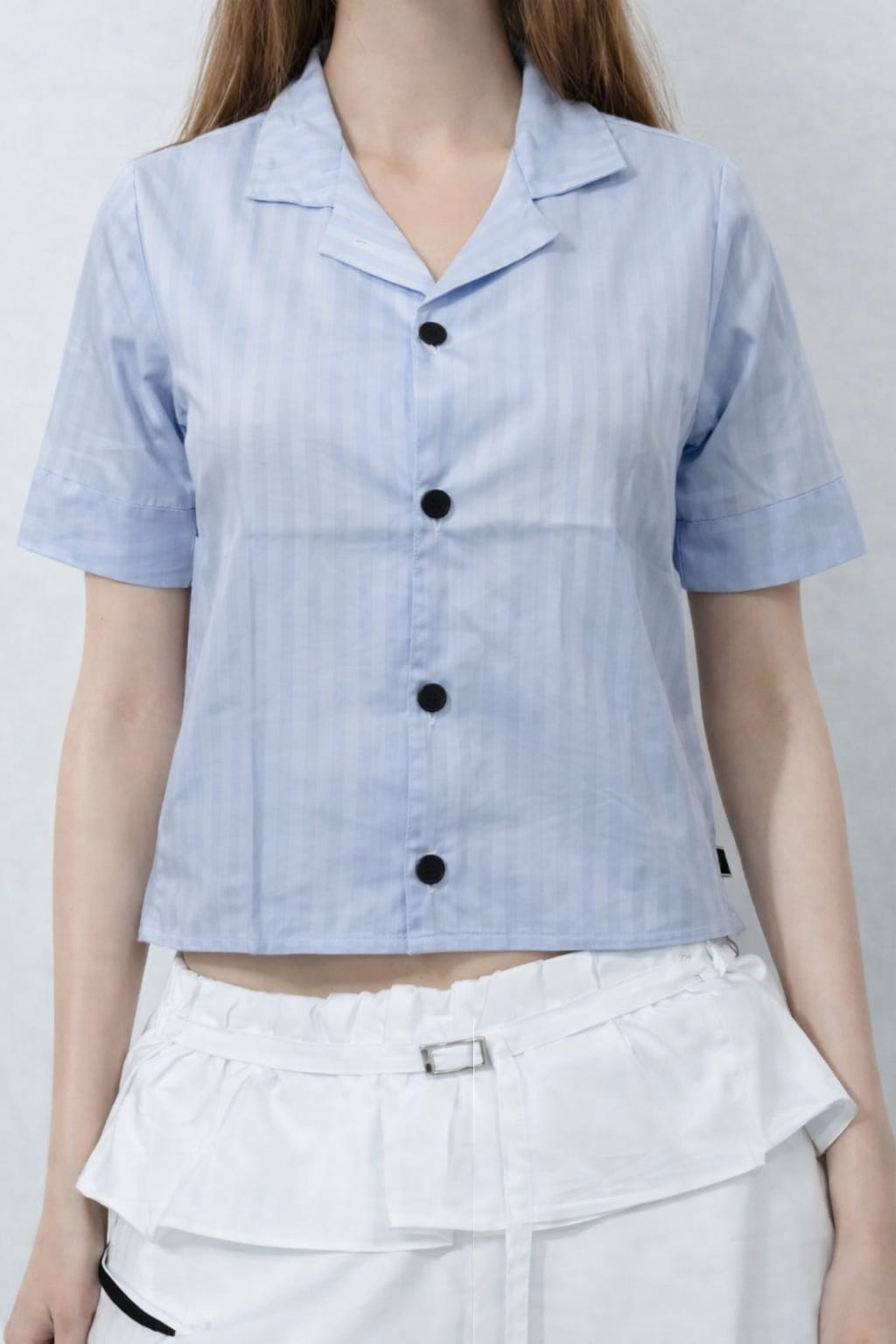 Light blue striped shirt with black buttons worn by a person on a plain background