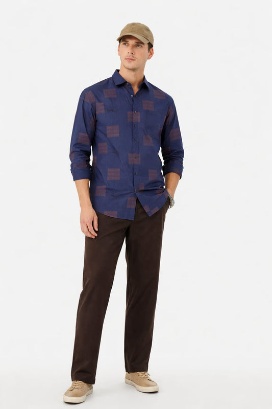 Man wearing a blue patterned shirt and brown pants on a white background