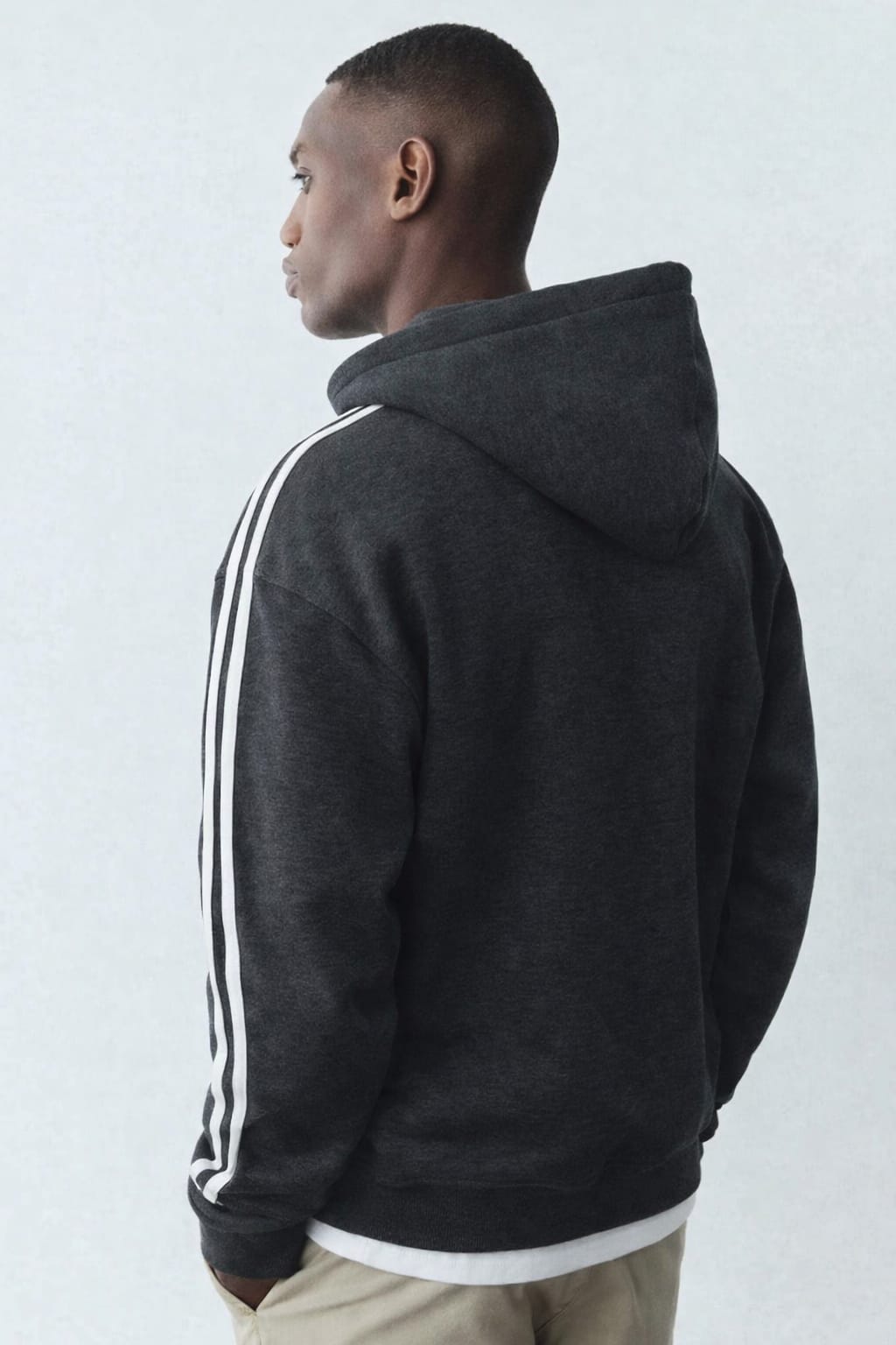 Person wearing a dark gray hoodie with white stripes on a light gray background
