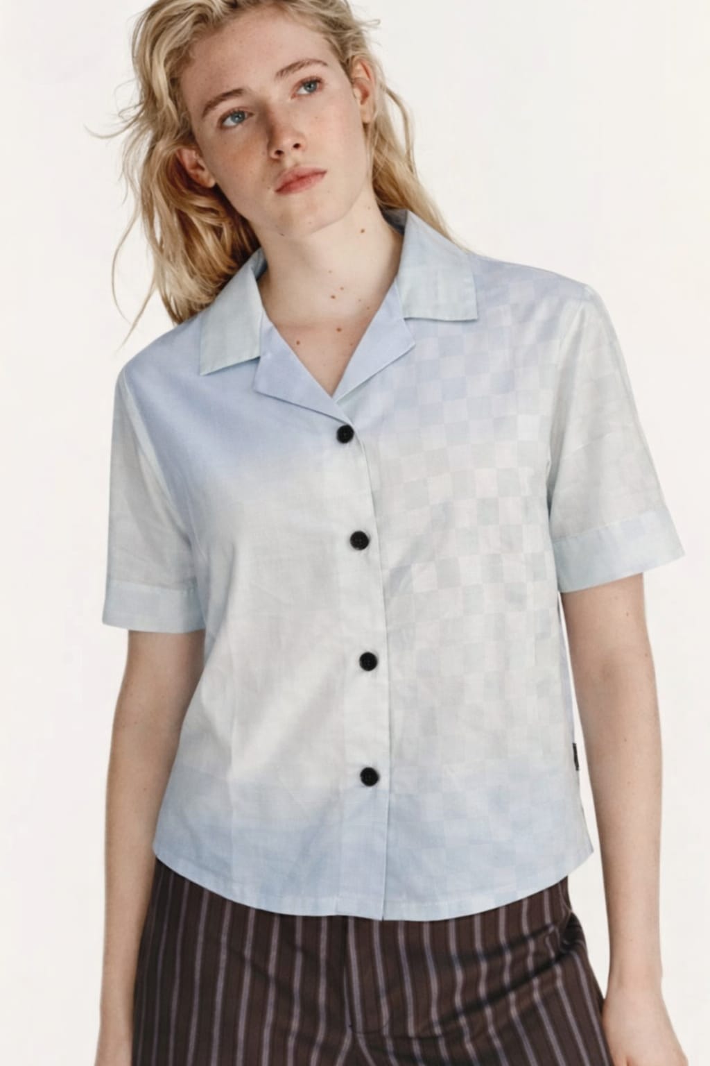 Woman wearing a light blue short-sleeve shirt with black buttons on a white background