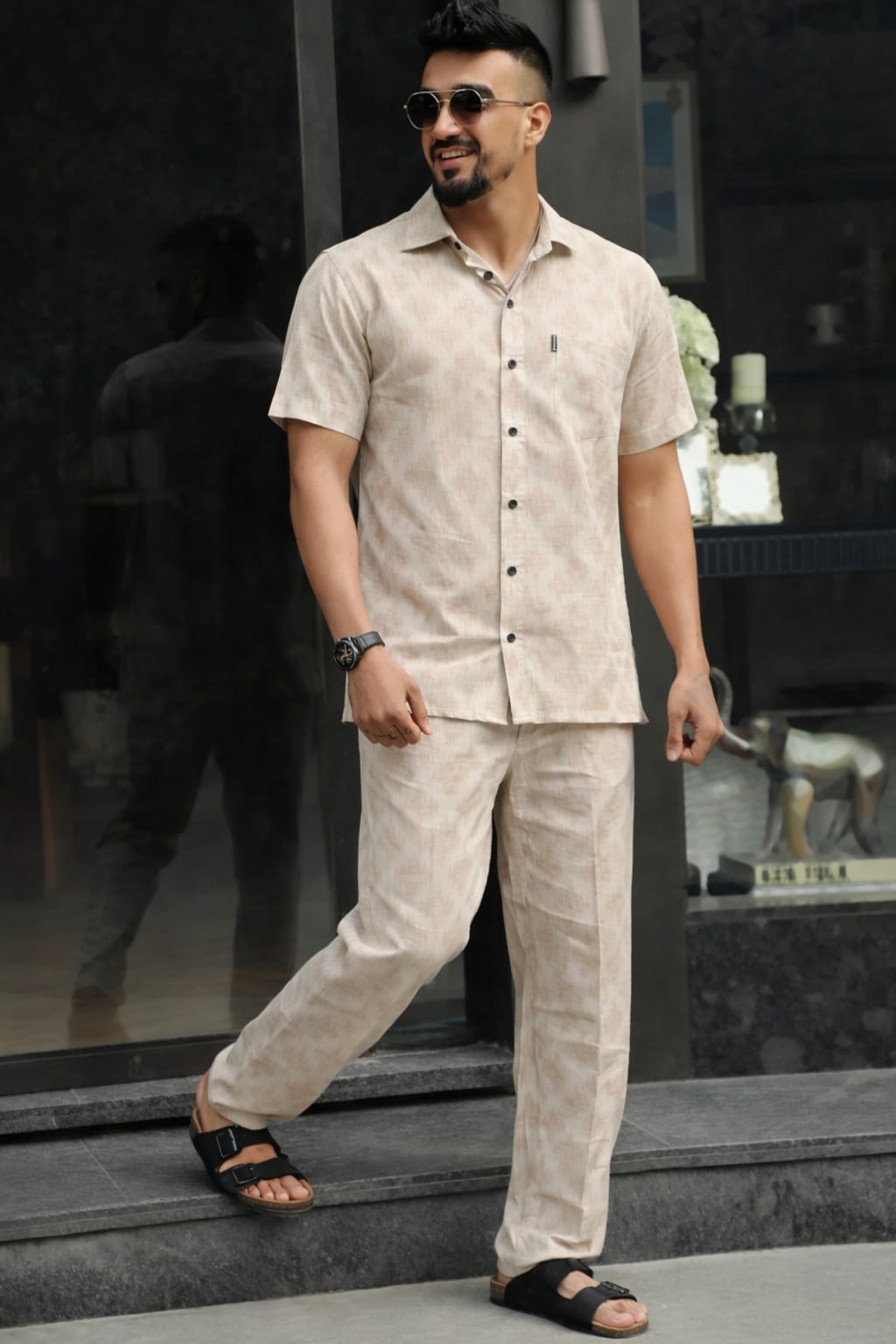 Man wearing a beige linen outfit with sunglasses, standing on steps.