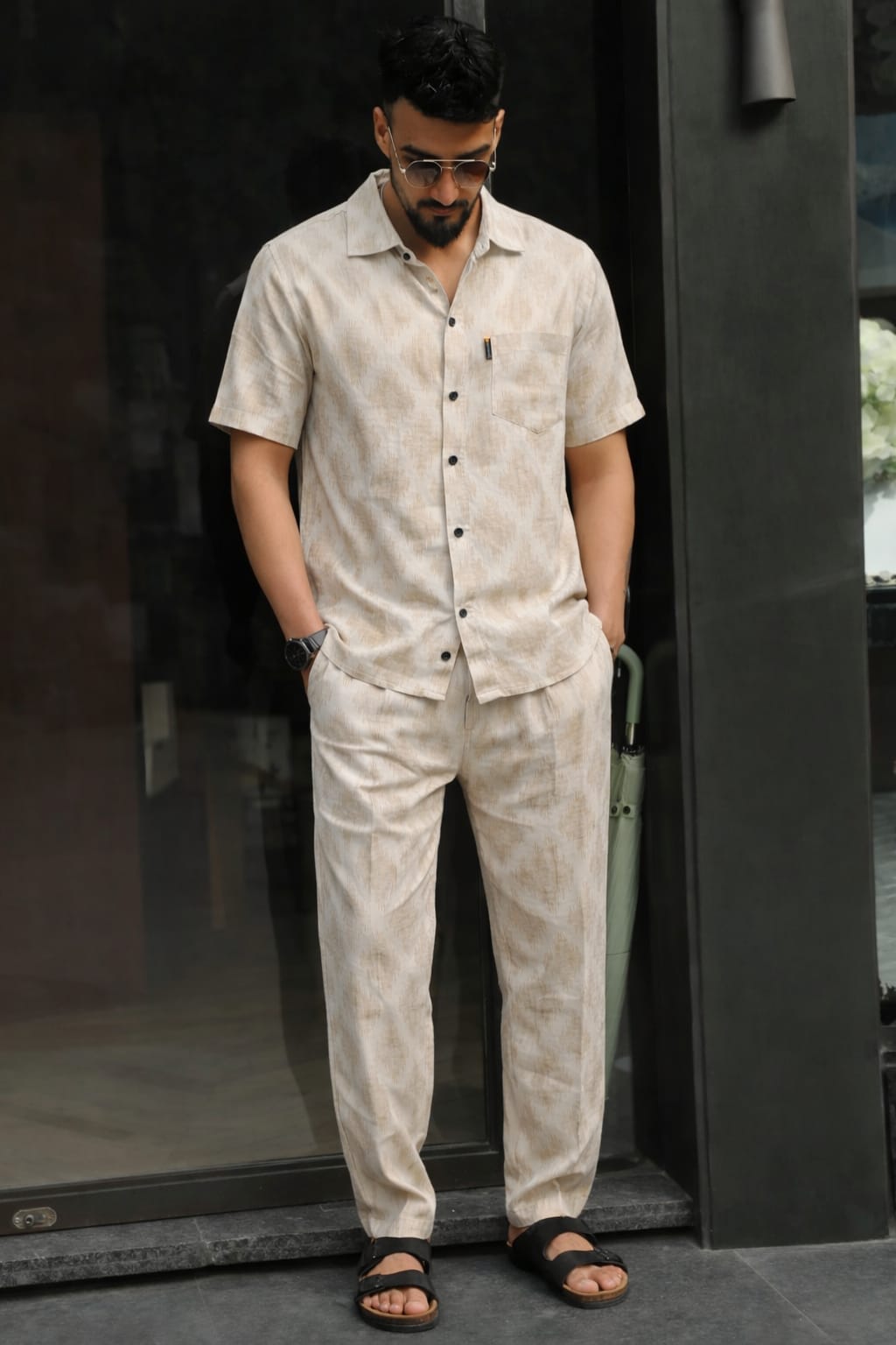 Man wearing a beige button-up shirt and pants standing against a dark background