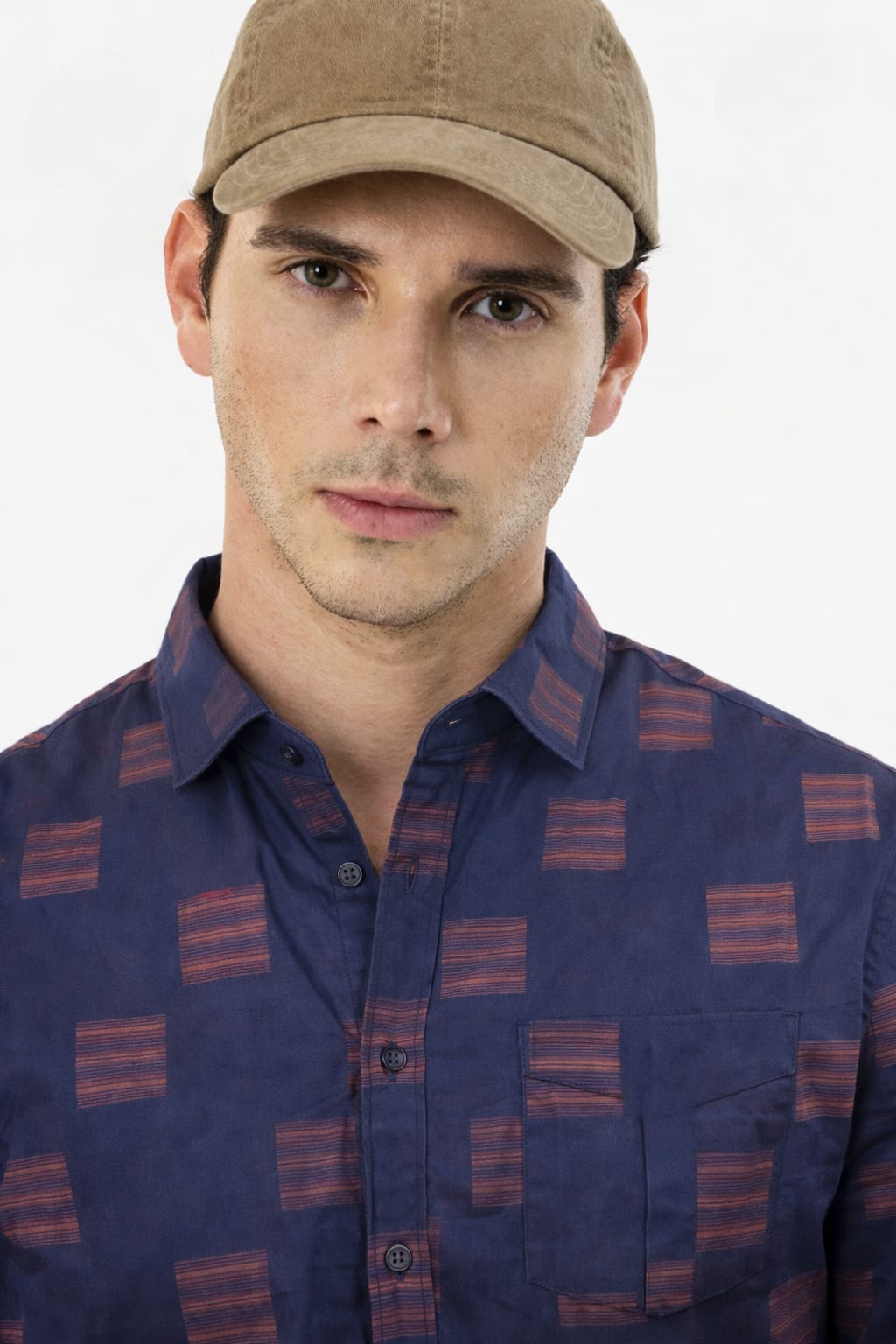Man wearing a patterned shirt and beige cap on a white background