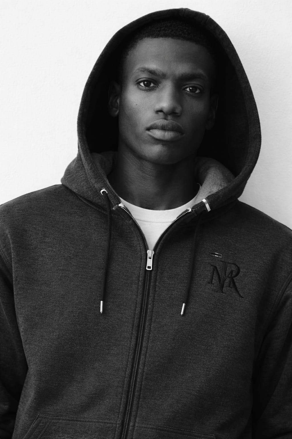 Person wearing a dark hoodie with a logo on a white background