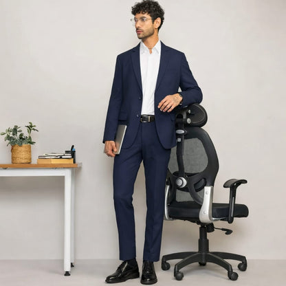 Man in a navy suit standing next to an office chair in a minimalistic office setting